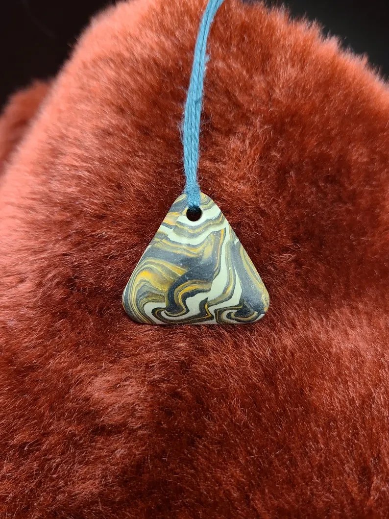 A triangular polymer clay pendulum, marbled in gold, indigo and cream, on a sky-blue cord